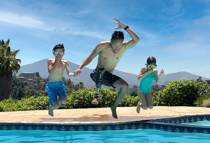 father with prosthetic leg jumping into a pool with his kids